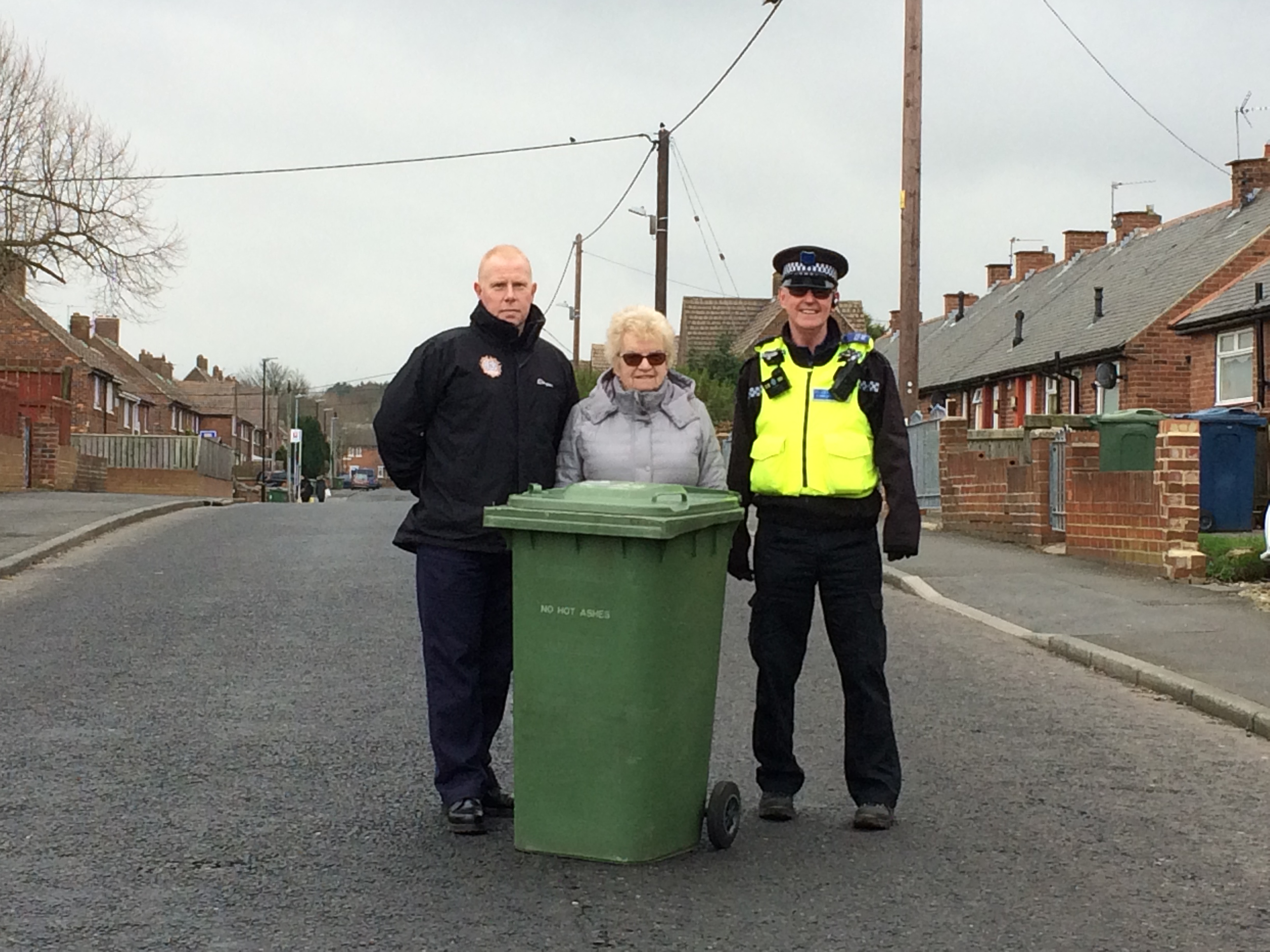 Firefighter councillor and PCSO stand next to a wheelie bin