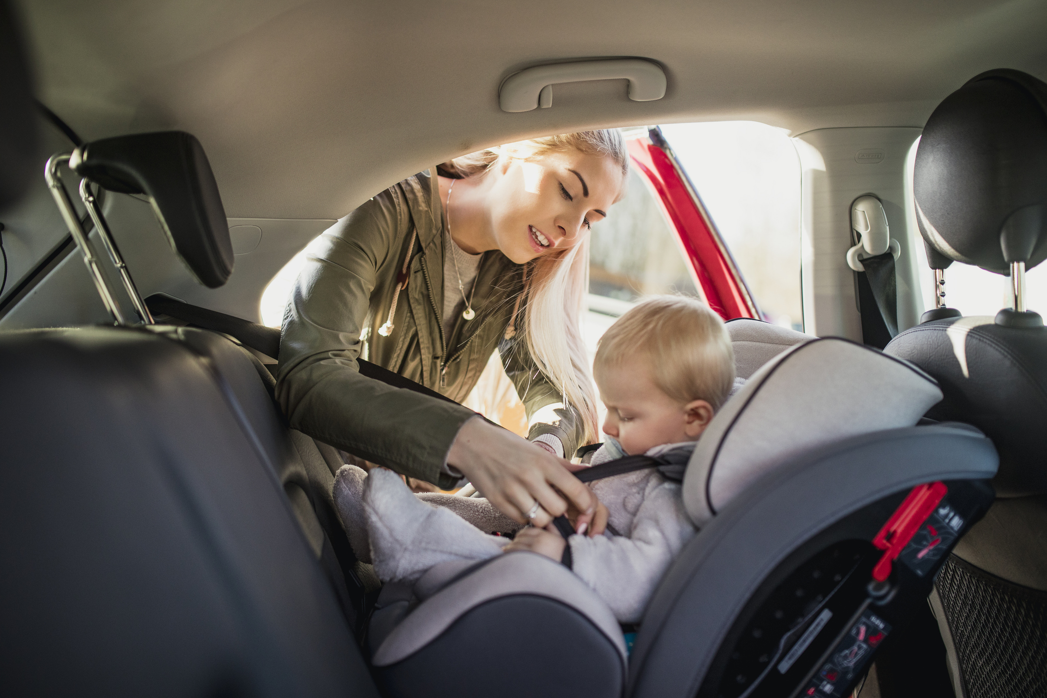 Young Mother putting her son in a car seat.