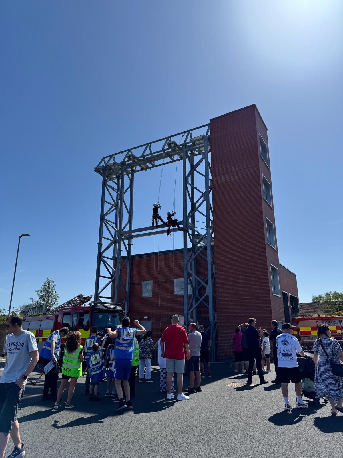 Firefighters performing rope rescue demonstration, abseiling from structure in front of crowd